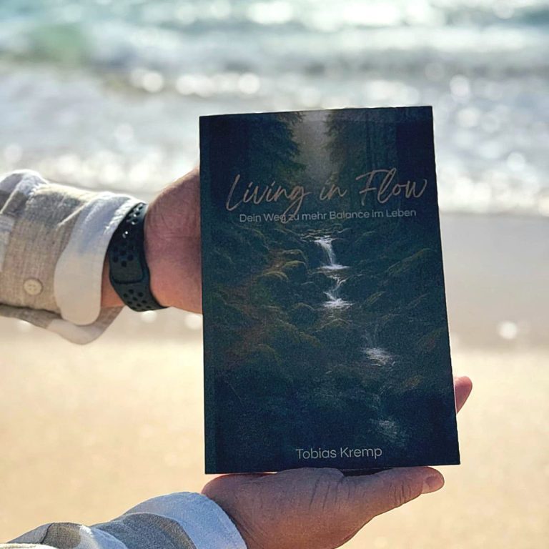 Ein Buch liegt im Wald auf moosbedecktem Boden, umgeben von Bäumen und einem kleinen Bach.